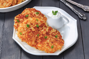 Vegetable fritters. Pancakes with cabbage, green onion and yogurt dressing on white plate. Dark wooden background, close-up