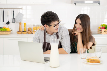 Young Asian couple play laptop in white kitchen and enjoying breakfast.