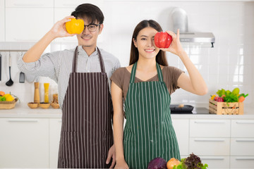 Young Asian couple holding vegetable for prepare cooking food in the white kitchen.