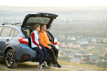 Happy couple standing together near a car with open trunk enjoying view of rural landscape nature....