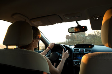 Close up view of a woman driver holding steering wheel driving a car at sunset.
