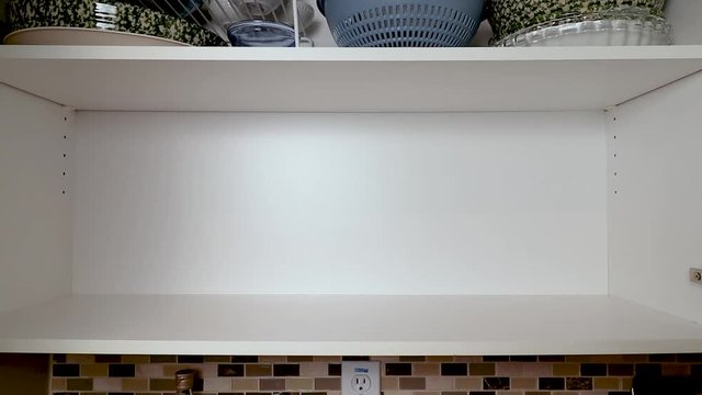 Person opening cabinet and neatly stacking clean plates and other colorful dishware. 