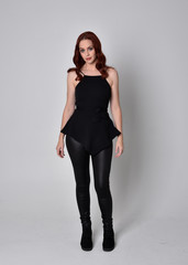 portrait of a pretty girl with red hair wearing black leather pants and top. Full length standing...