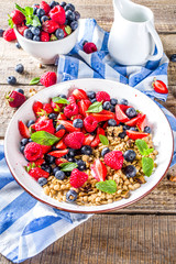 Healthy morning food, Breakfast oatmeal granola or muesli with various berry and milk, yogurt, wooden rustic background. Woman hands hold plate, sppon, flatlay top view