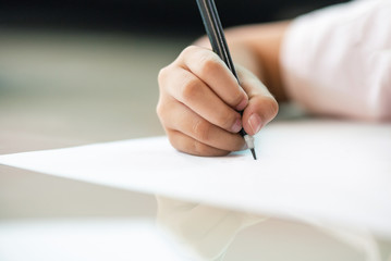 Close up image of a child is using a black pencil to write or draw something on white paper.