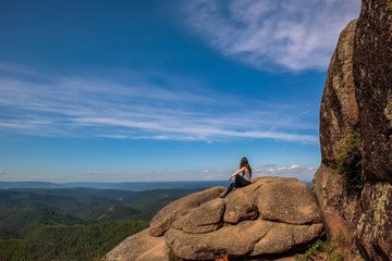 Girl alone sitting on a rock at Stolby Nature Sanctuary in Siberian Russia, into the wild