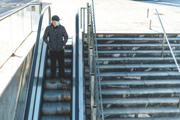 Caucasian man, with mask on his face, standing on a escalator