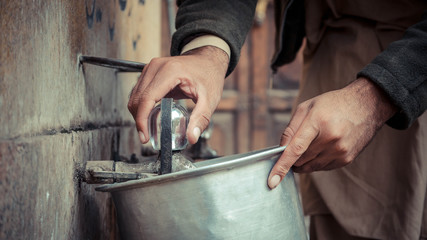 Hand Turning Water Tap While Holding Metal Pot