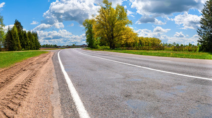 Asphalt road panorama in countryside on sunny summer day against a blue sky with snow-white clouds