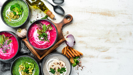 Set of colored soups on white wooden background. Beet soup, broccoli cream soup and mushroom soup. Top view.