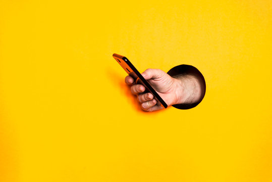 Male Hand From A Hole In A Paper Wall Holding A Smartphone With A Black Screen.Business Background