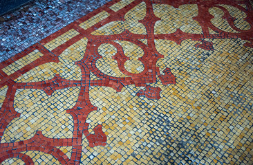 Old, worn out well used small mosaic floor tiles in ornate pattern of Blue, Yellow and red.