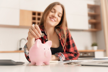 Obraz na płótnie Canvas Woman putting money into piggy bank at table