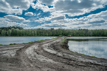 Dirt road towards forest and clouds