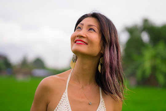 outdoors holidays portrait of attractive and happy middle aged Asian Korean woman in white dress enjoying freedom and nature at green field landscape carefree and cheerful