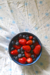 Bowl of blueberries and strawberries on a bed. Top view.