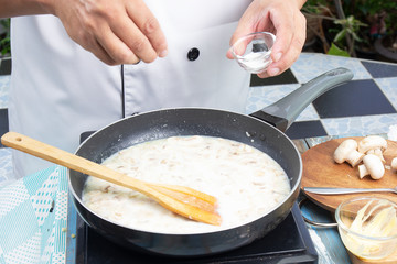 Chef putting salt in the pan for cooking mushroom cream soup