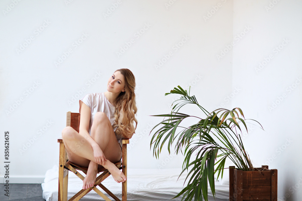 Wall mural portrait of a beautiful slender girl with blond hair sitting on a chair.