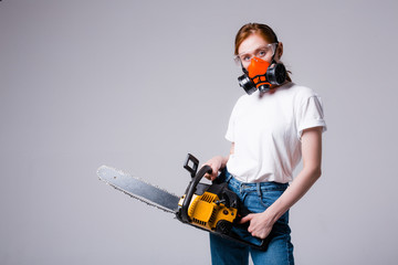 Red-haired girl in white T-shirt in construction respirator and goggles holds a chainsaw. Advertising banner for a hardware store