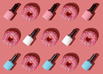 Creative pattern of donuts in pink glaze with multicolored pastry sprinkles and bottles of nail...