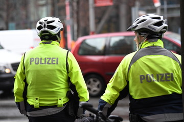Unrecognizable back turned German policemen with helmets and yellow reflective jacket riding bikes