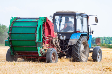 tractor makes big straw roll on yellow field at summer day