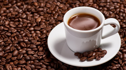 A cup of coffee, stands on coffee beans.