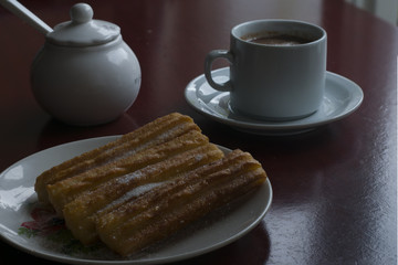 A cup with chocolate and milk and a plate with some traditional spanish churros. Spanish breakfast.