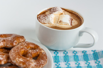fragrant gingerbread cookies on a white plate with a cup of warm cocoa or coffee with marshmallow, sprinkled with chocolate, white background, blue napkin, delicious dessert, feeling of comfort