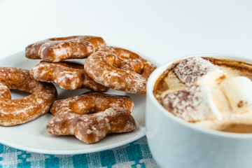 fragrant gingerbread cookies on a white plate with a cup of warm cocoa or coffee with marshmallow, sprinkled with chocolate, white background, blue napkin, delicious dessert, feeling of comfort