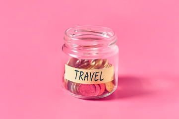 Glass jar with coins and inscription travel lies on pink background. Concept paying for journey