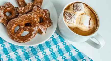 fragrant gingerbread cookies on a white plate with a cup of warm cocoa or coffee with marshmallow, sprinkled with chocolate, white background, blue napkin, delicious dessert, feeling of comfort