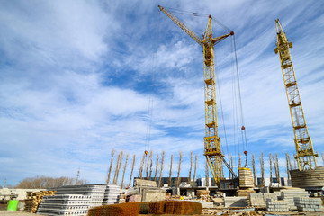 Naklejka premium Photos of high-rise construction cranes and an unfinished house against a blue sky. Photographed on a wide angle lens