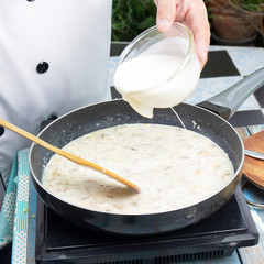 Chef pouring whipping cream in the pan for cooking mushroom cream soup
