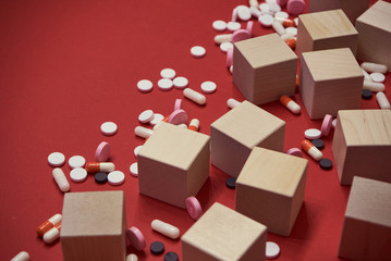 medical pills and wooden cubes scattered on red background