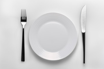 Table setting with a white plate next to cutleries on a white background. To represent a concept of healthy nutrition or an illustration for your product 