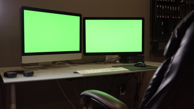 Panning view of dual screen computer with green screen at desk moving on slider.