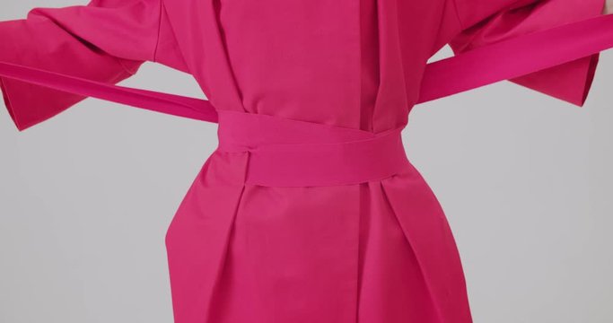 Studio shot of unrecognizable fashion model in pink dress/shirt making a bow of her belt/ribbon and posing. Tender hands with long fingers and pink manicure.  Wonderfull fuchsia colour
