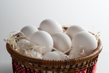 Close-up of a wicker basket lined with hay and filled with fresh and selected white chicken eggs....