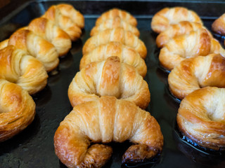 Freshly baked croissant at home, puff pastry present and melted butter at the bottom of the cookie sheet
