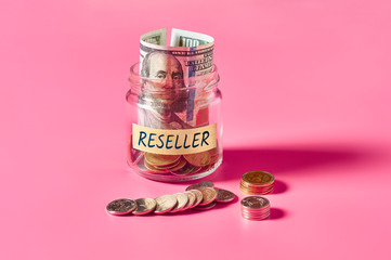 Glass jar with coins and inscription reseller lies on pink background