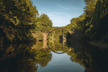 Rakotz bridge Rakotzbrucke also known as Devil's Bridge in Kromlau, Germany. Reflection of the bridge in the water create a full circle. Beautiful summer day with blue sky and clouds.