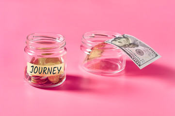 Glass jar with coins and inscription journey lies on pink background