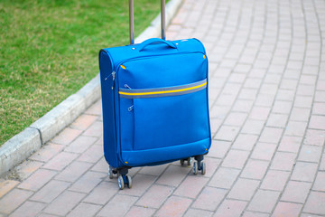 Fototapeta na wymiar Blue carry on suitcase with wheels and metal handle stands on the peron of the station. Passenger fast train in the background blurred. Travel concept
