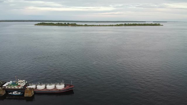 Aerial view. A barge moored to the shore of a wide river near the island at sunset. Cargo ship transporting sand on a navigable river.