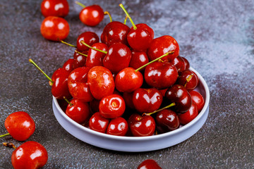 Sweet red cherries in a plate on dark background.