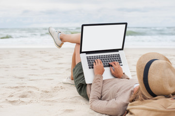 Young woman using laptop computer on a beach, white blank, empty screen monitor, Freelance work,...