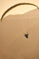Paralotniarz leci na paralotni, w tle piękny krajobraz i pomarańcz zachodzącego słońca