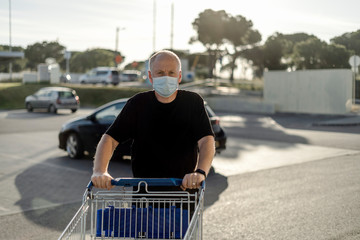 Man wearing protective facial mask pushing shopping cart