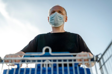 Man wearing protective facial mask pushing shopping cart